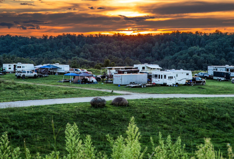 An expansive view of a campground with various RVs and trailers set against a vibrant sunset and forested hills